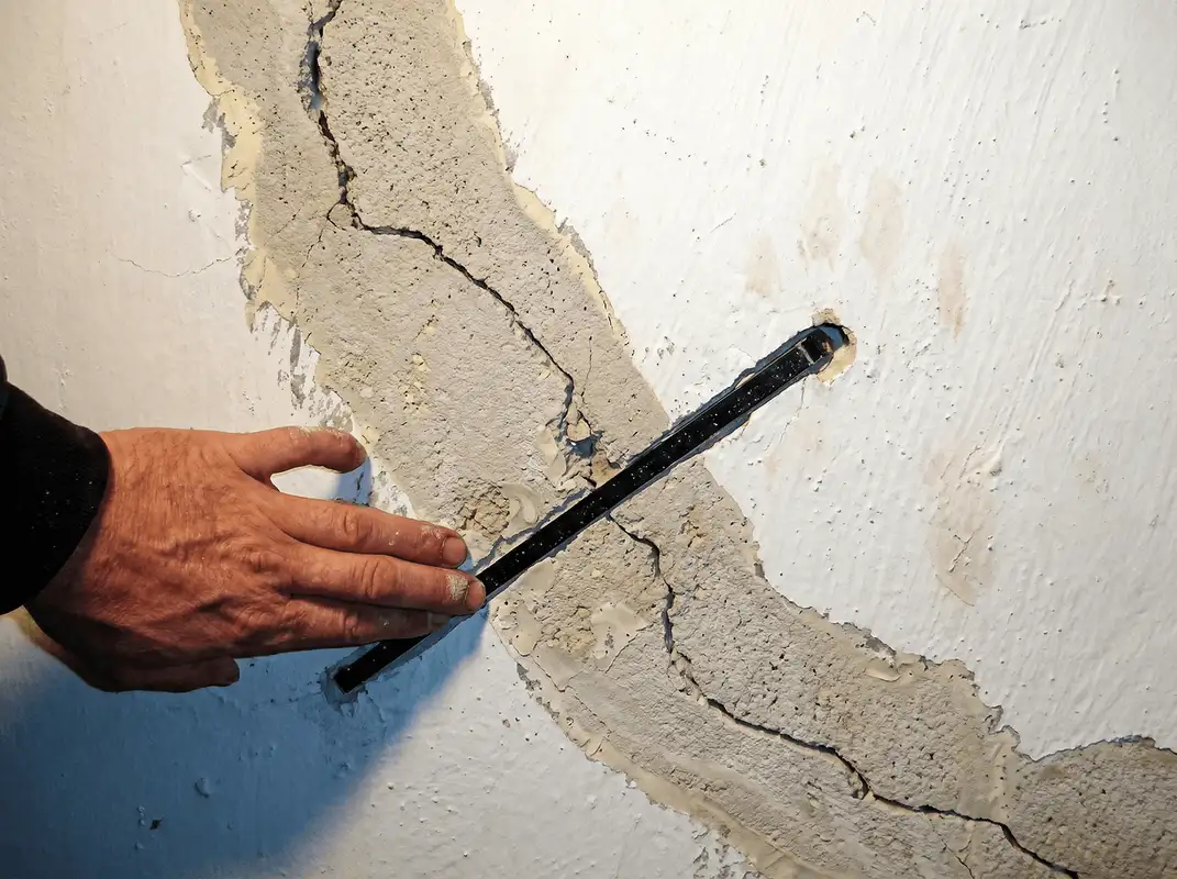 A wall with a large crack is being inspected by a professional in Bloomington, IN